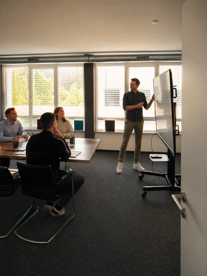 Vier Personen in einer Schulung im Besprechungsraum, ein Trainer erklärt am Whiteboard
